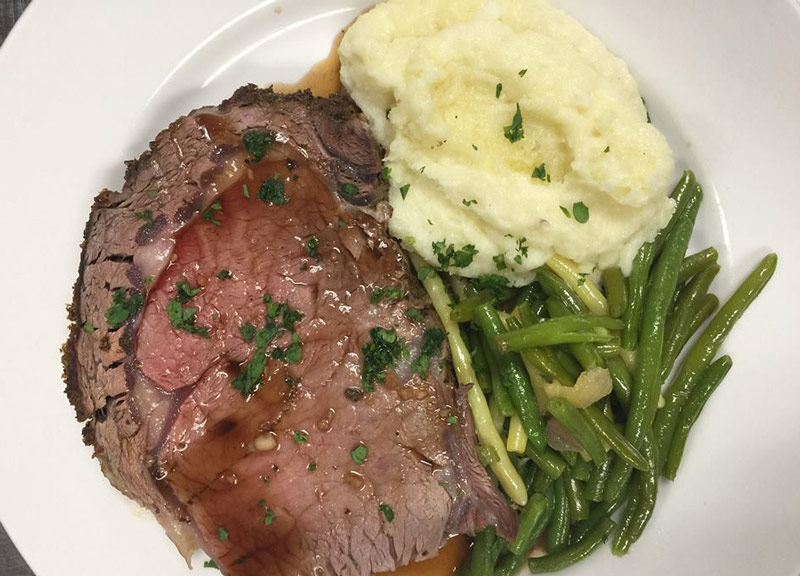 A plate of prime rib, mashed potatoes, and green bean almandine