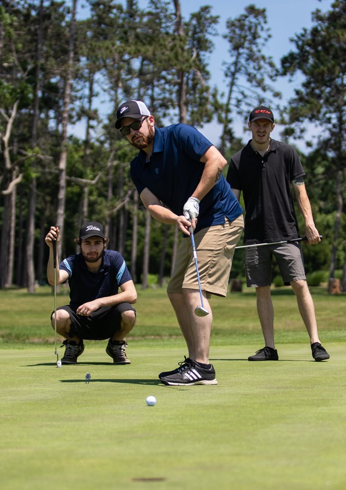 three golfers watching putt move towards hole